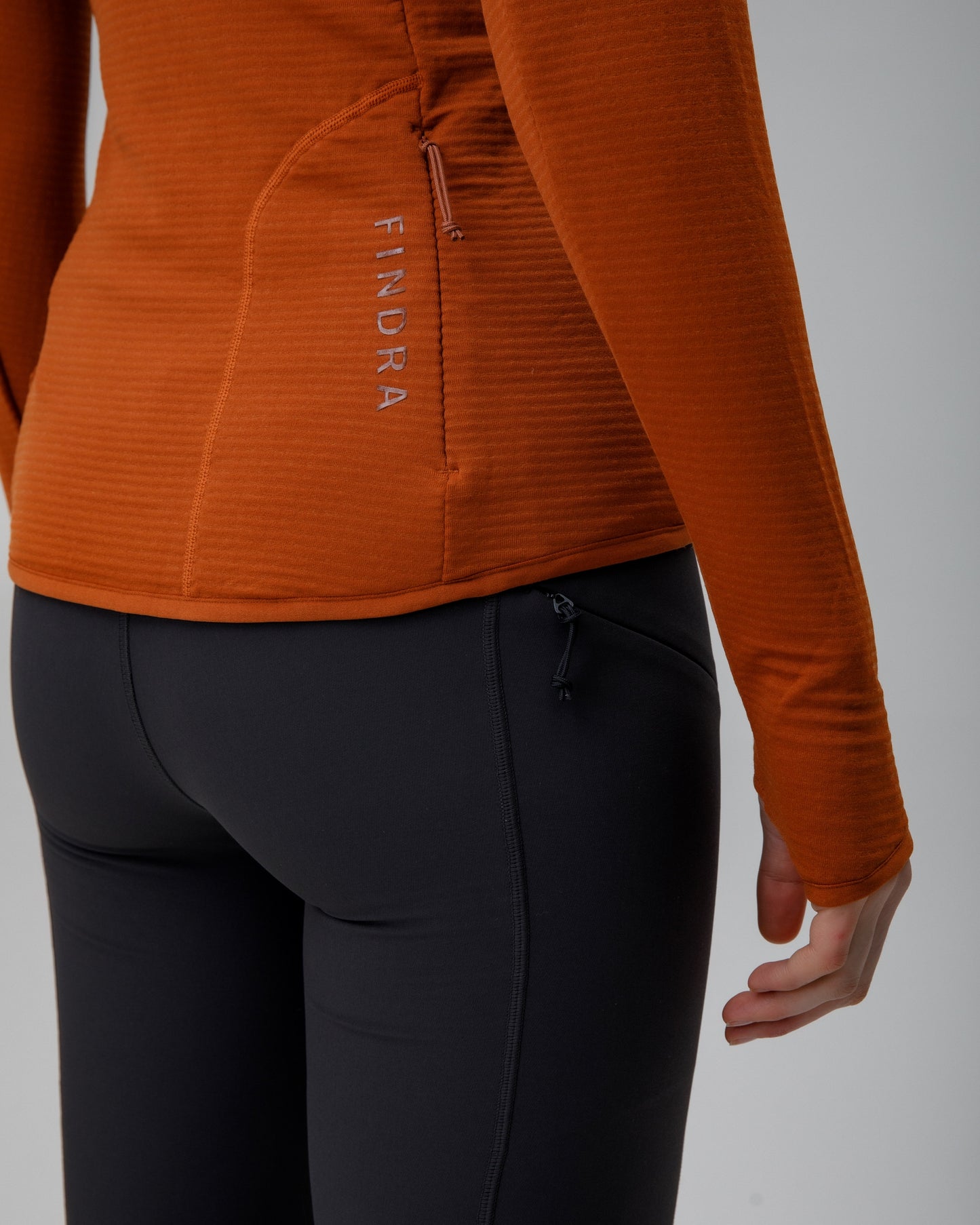 Person wearing an orange long-sleeve shirt and black pants on a gray background
