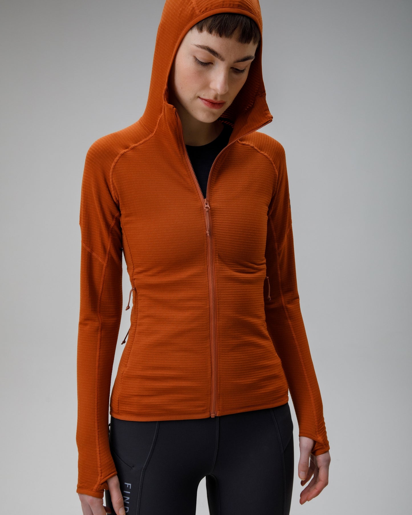 Person wearing an orange hooded jacket on a gray background