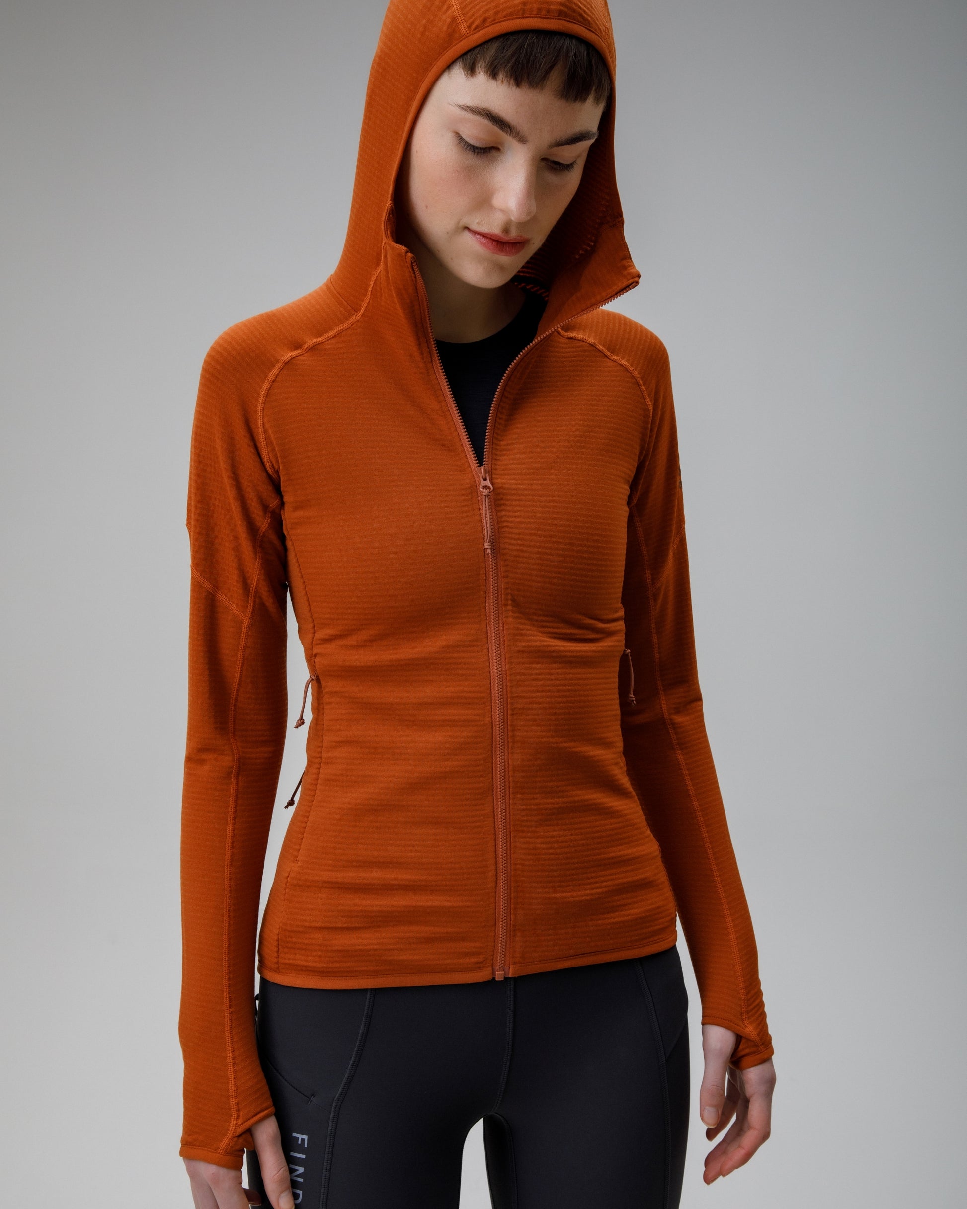 Person wearing an orange hooded jacket on a gray background