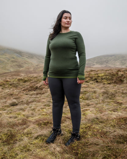 Person wearing a green long-sleeve top and black leggings standing in a misty mountain landscape.