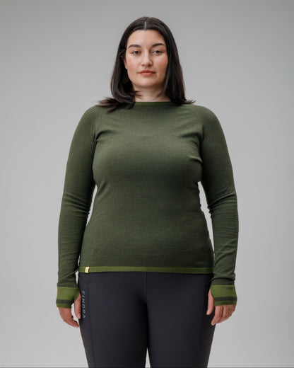 Woman wearing a green long-sleeve top and black leggings against a gray background