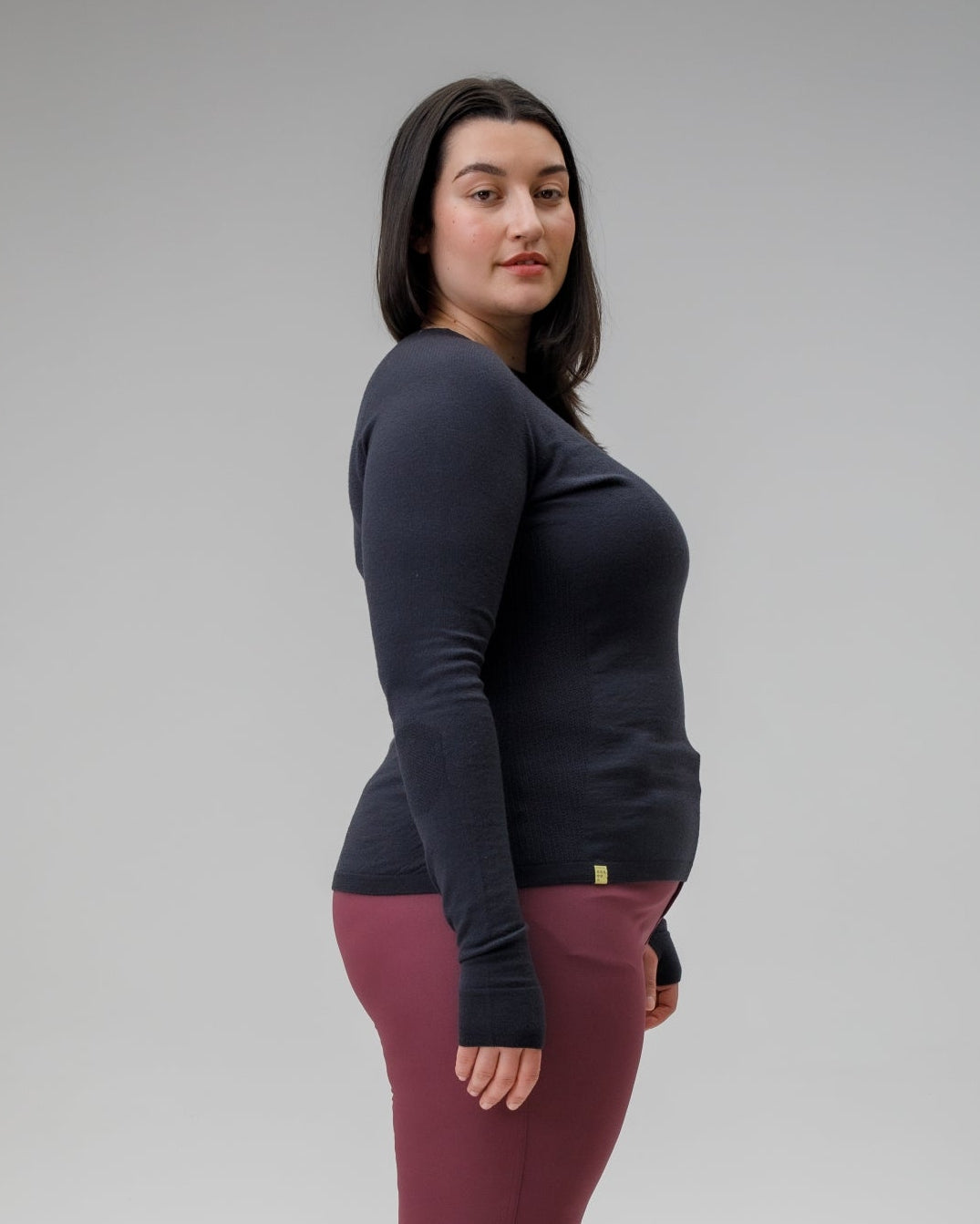 Woman wearing a dark long-sleeve top and maroon pants on a gray background