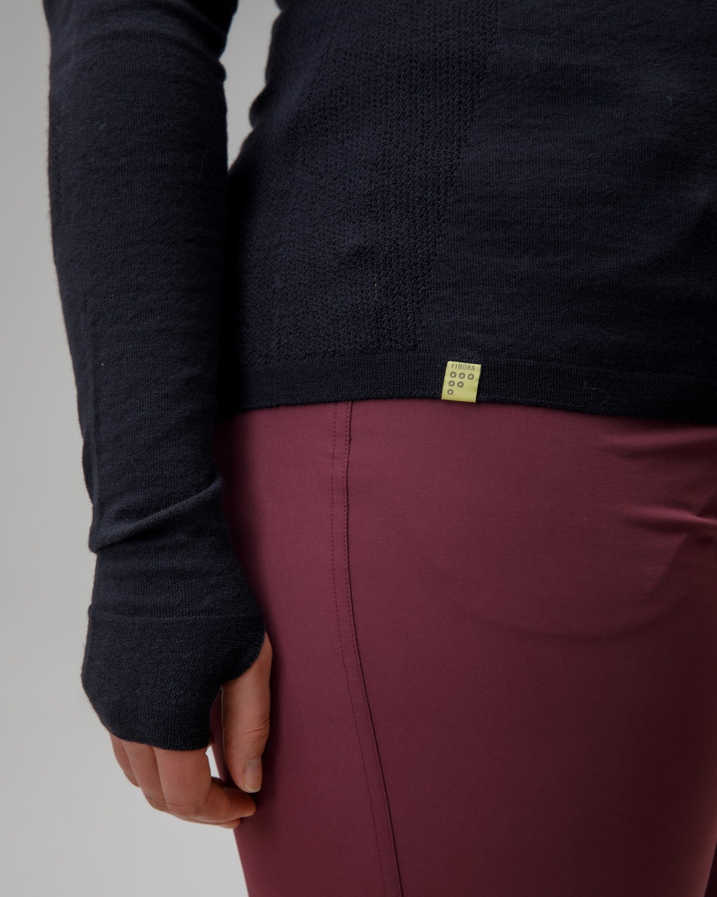 Person wearing a dark long-sleeve shirt and maroon pants with a visible brand logo on a gray background
