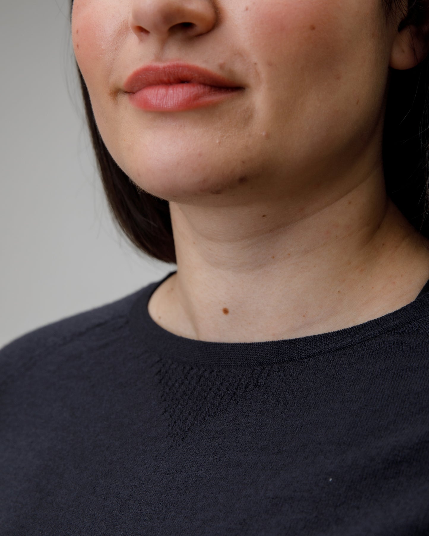 Close-up of a person wearing a charcoal grey merino base layer with a neutral background