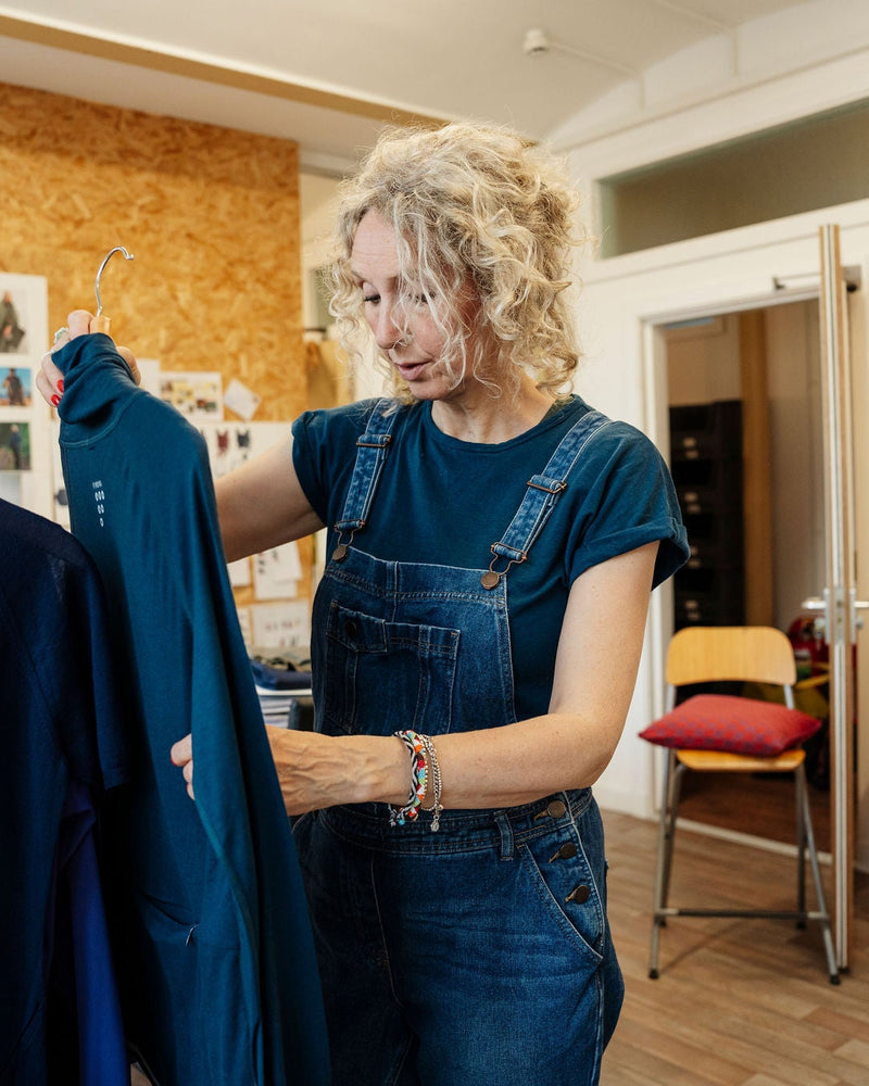 Alex Feechan, founder of FINDRA in a clothing store holding a teal shirt next to a rack of clothes.