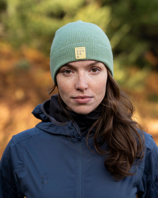 Person wearing a green beanie with a logo and a blue jacket outdoors.
