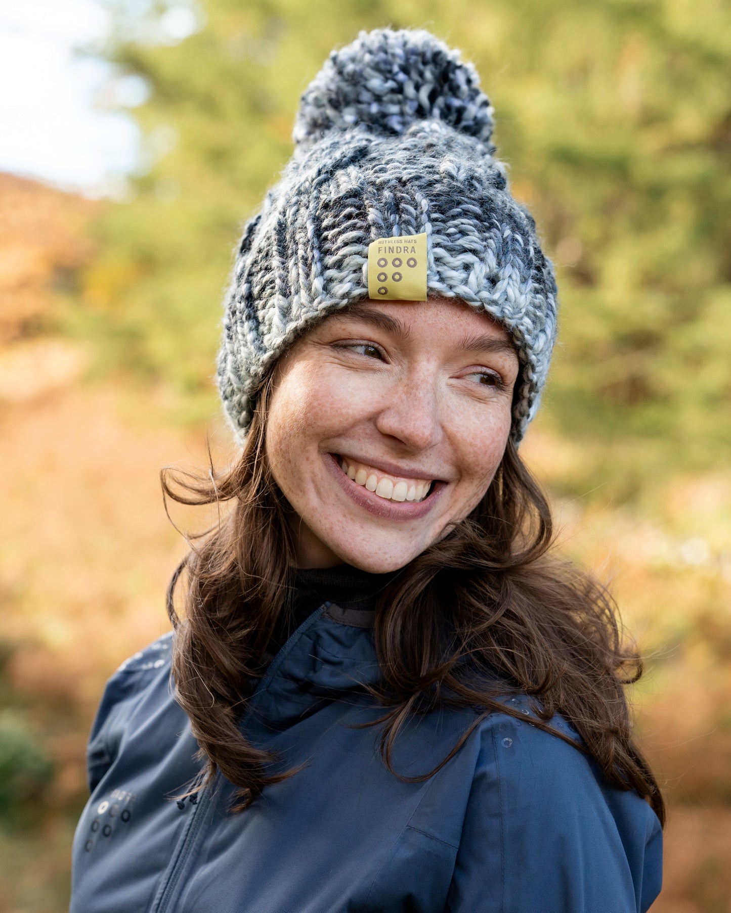 Woman wearing a blue jacket and gray knit hat with a pom-pom outdoors