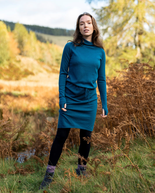 Woman in a teal merino wool dress standing in a natural setting with trees and grass.