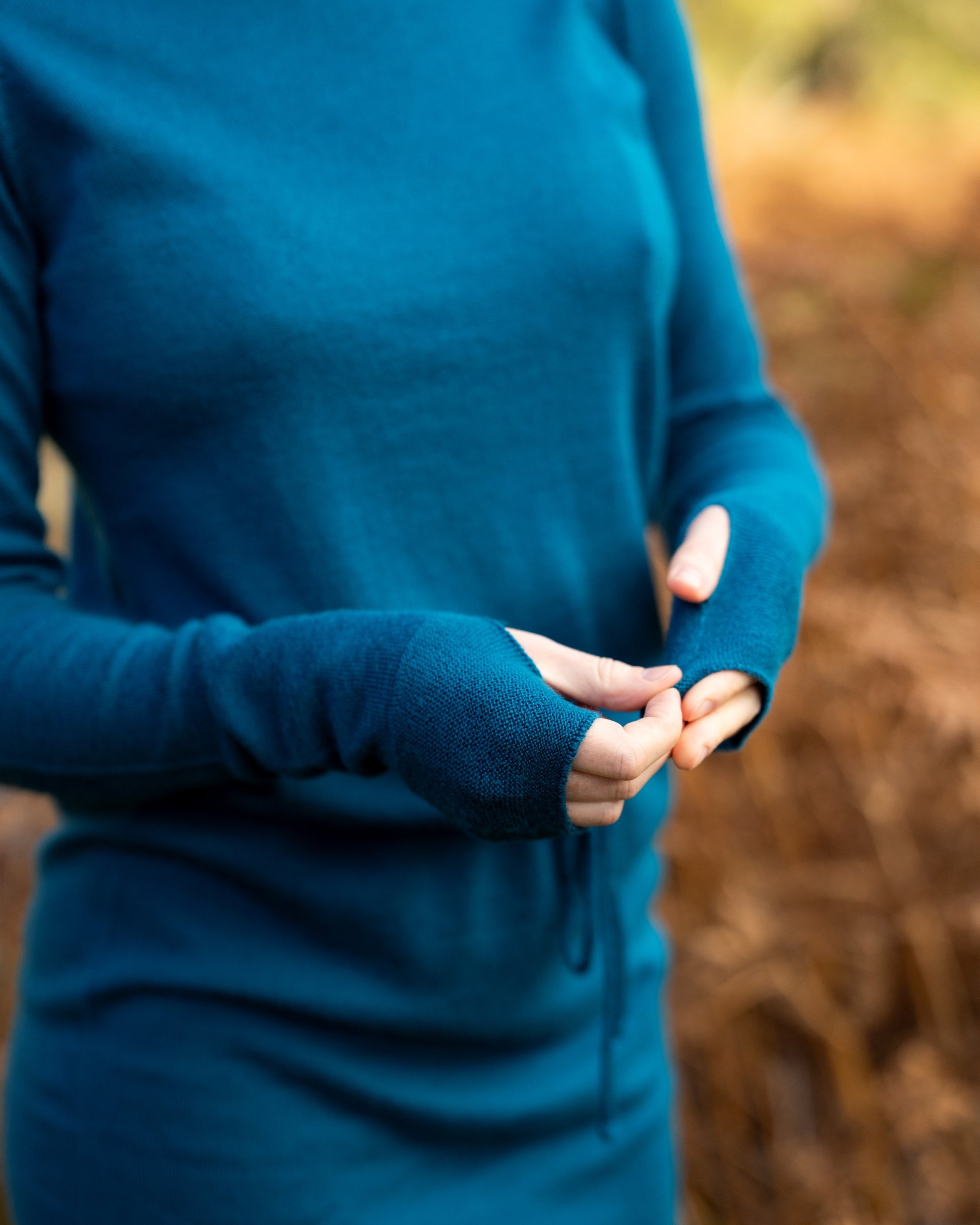 Person wearing a teal merino wool dress with thumb passes on the sleeve against a blurred natural background