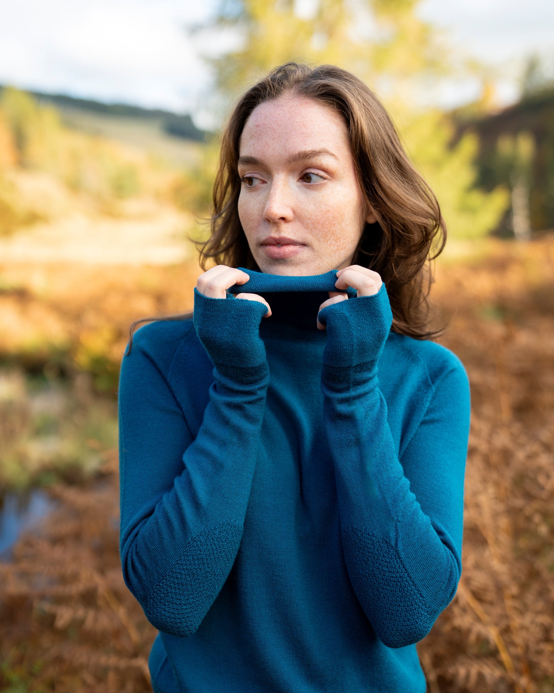 Woman wearing a teal merino wool dress in an outdoor setting with blurred background