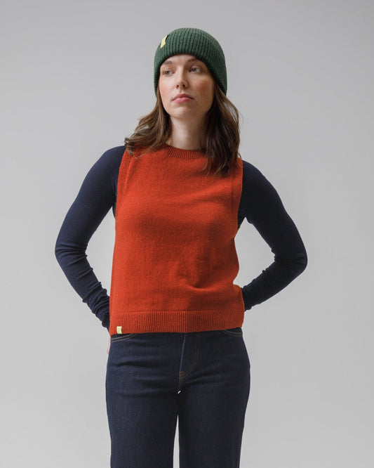 Person wearing a red vest, navy pants, and a green beanie on a gray background