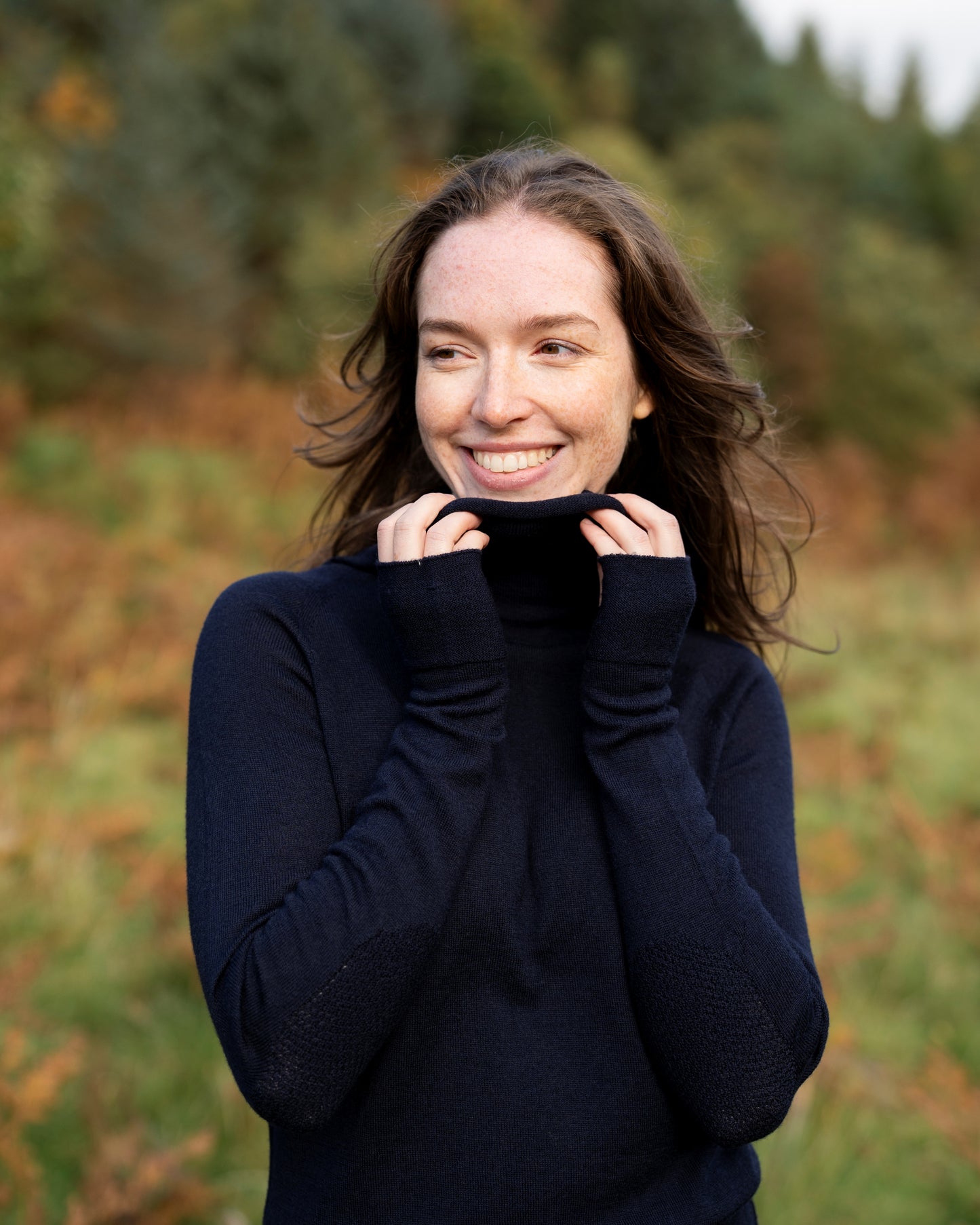 Woman wearing a dark navy cowl neck dress in a natural setting with trees and grass.