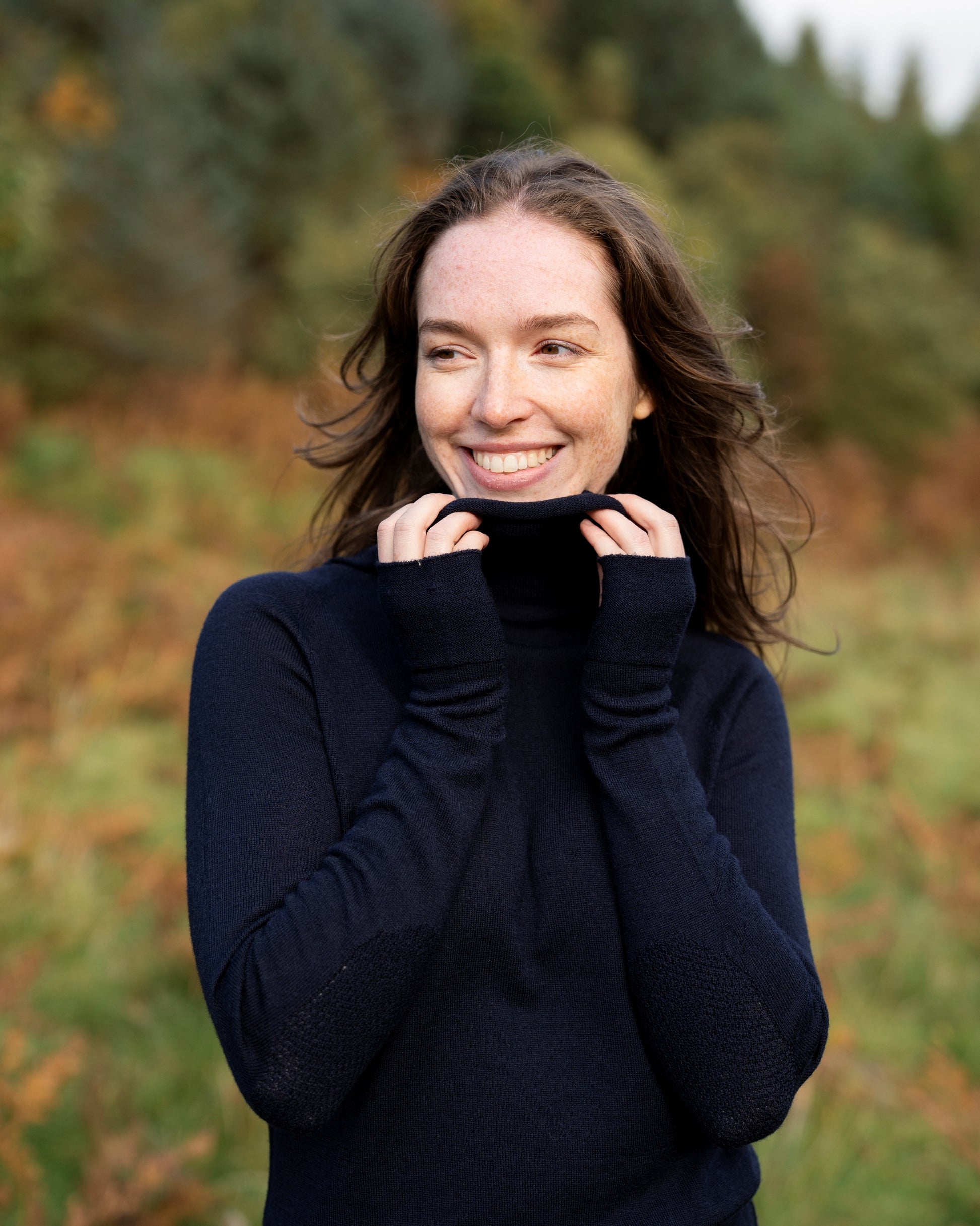 Woman wearing a dark navy cowl neck dress in a natural setting with trees and grass.