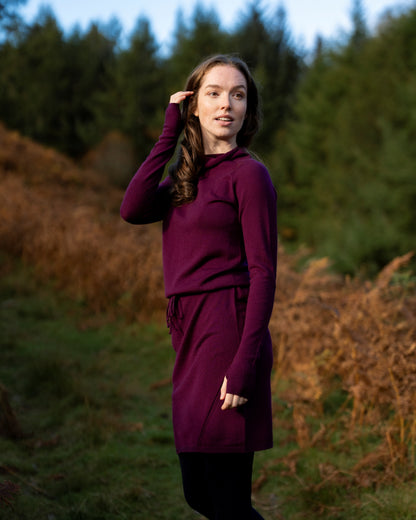 Woman in an eggplant merino wool dress  standing in a field with trees in the background