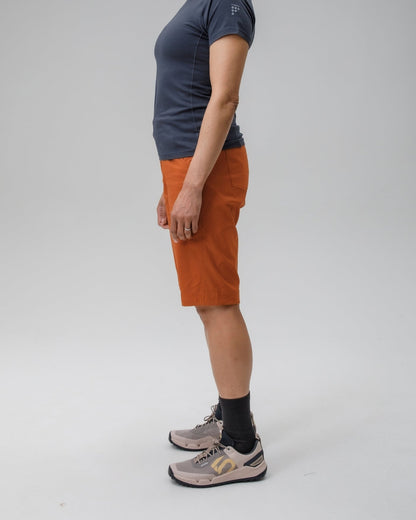 Person wearing a dark gray t-shirt and orange shorts standing against a plain background