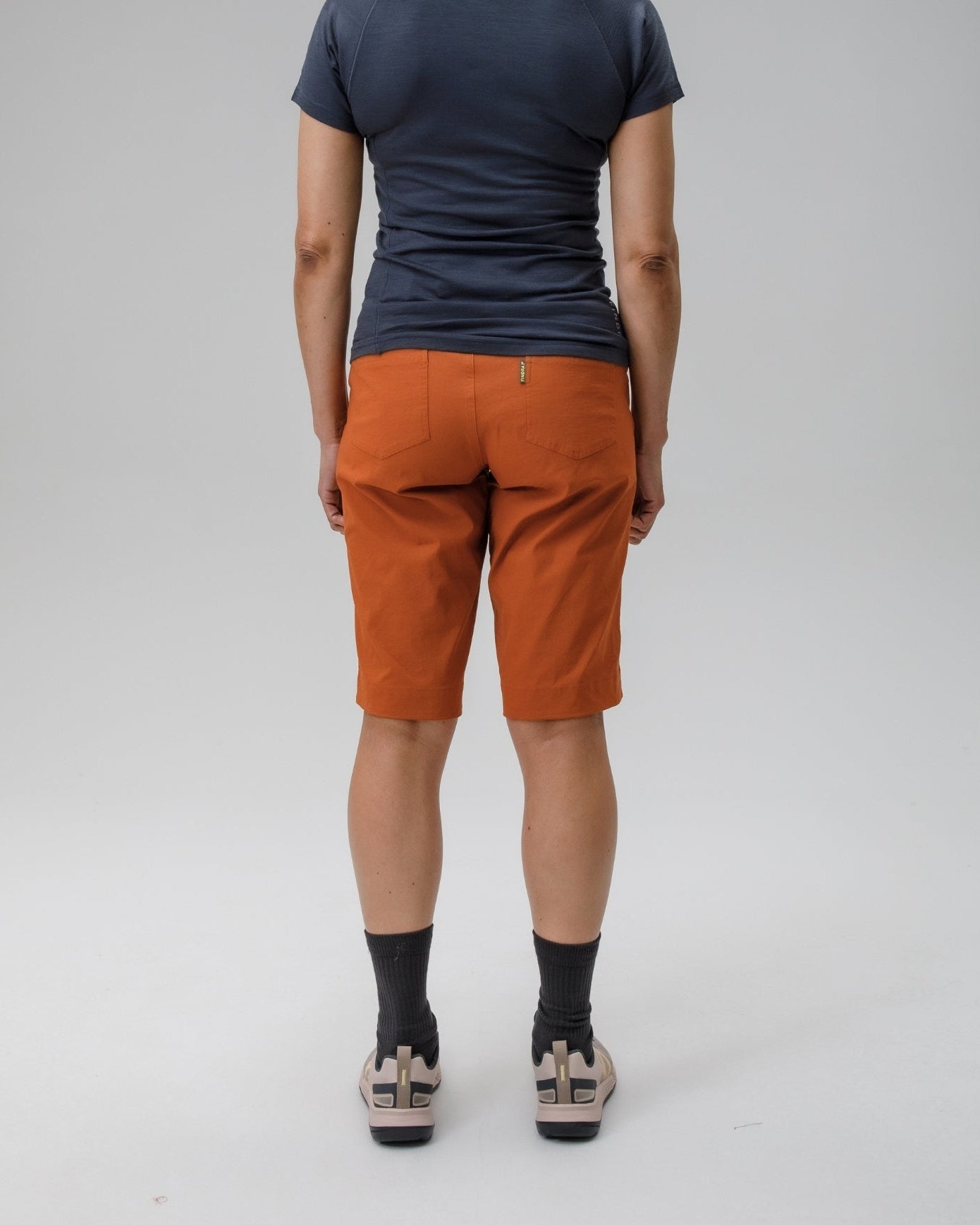 Person wearing a dark blue t-shirt and orange shorts on a gray background