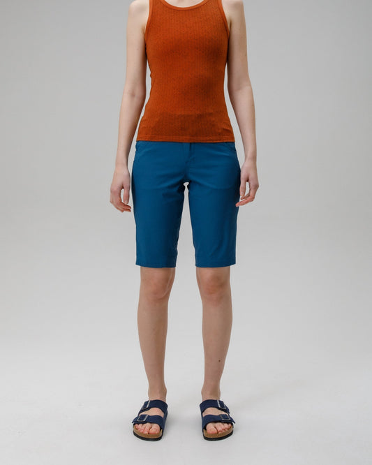 Person wearing a rust-colored sleeveless top and blue shorts on a gray background