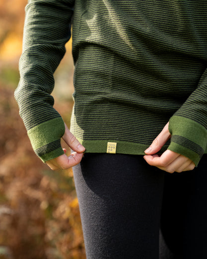 Person wearing a Moss green MErino wool base layer showing the FINDRA Logo on a yellow tag with a blurred natural background