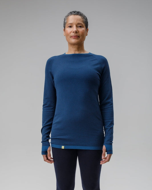 Person wearing a blue long-sleeve top and black leggings on a gray background