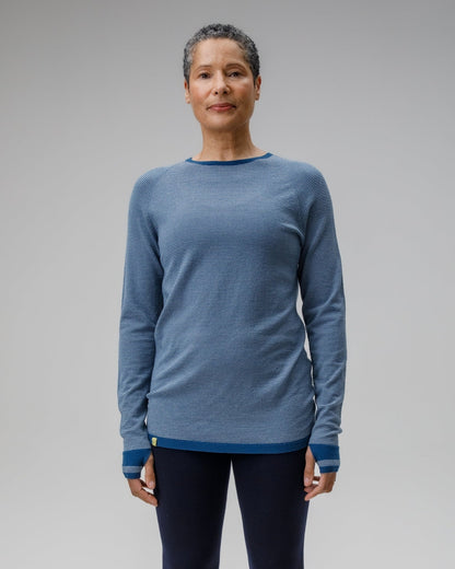 Person wearing a blue long-sleeve shirt and black leggings on a gray background