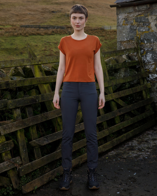 Woman in the scottish countryside wearing an orange merino t-shirt and graphite grey technical trousers. 