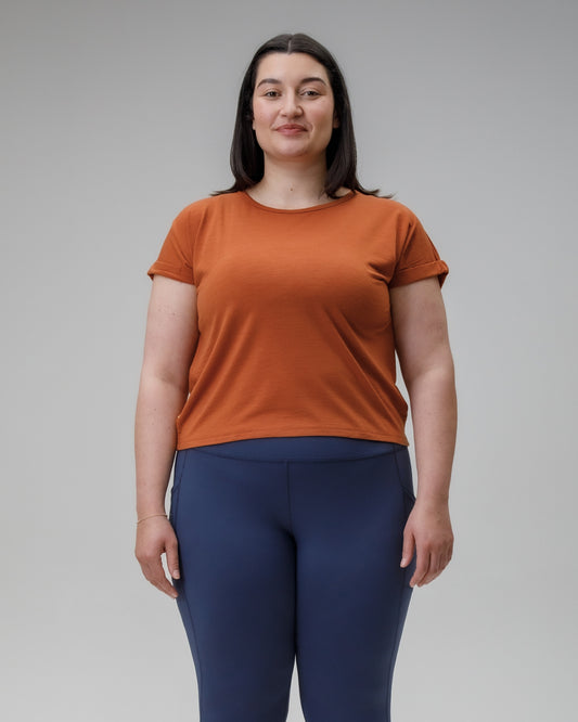 Woman wearing an orange t-shirt and blue leggings against a gray background