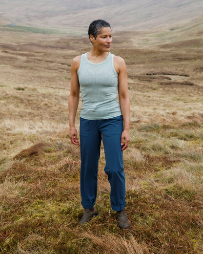 Person standing in a field wearing a light blue tank top and dark blue pants.