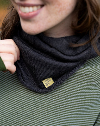 Person wearing a charcoal grey neck warmer in Merino wool with a visible brand tag, smiling outdoors.