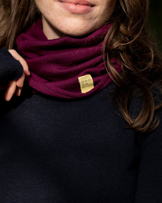 Woman wearing a dark blue sweater and maroon scarf with a blurred forest background