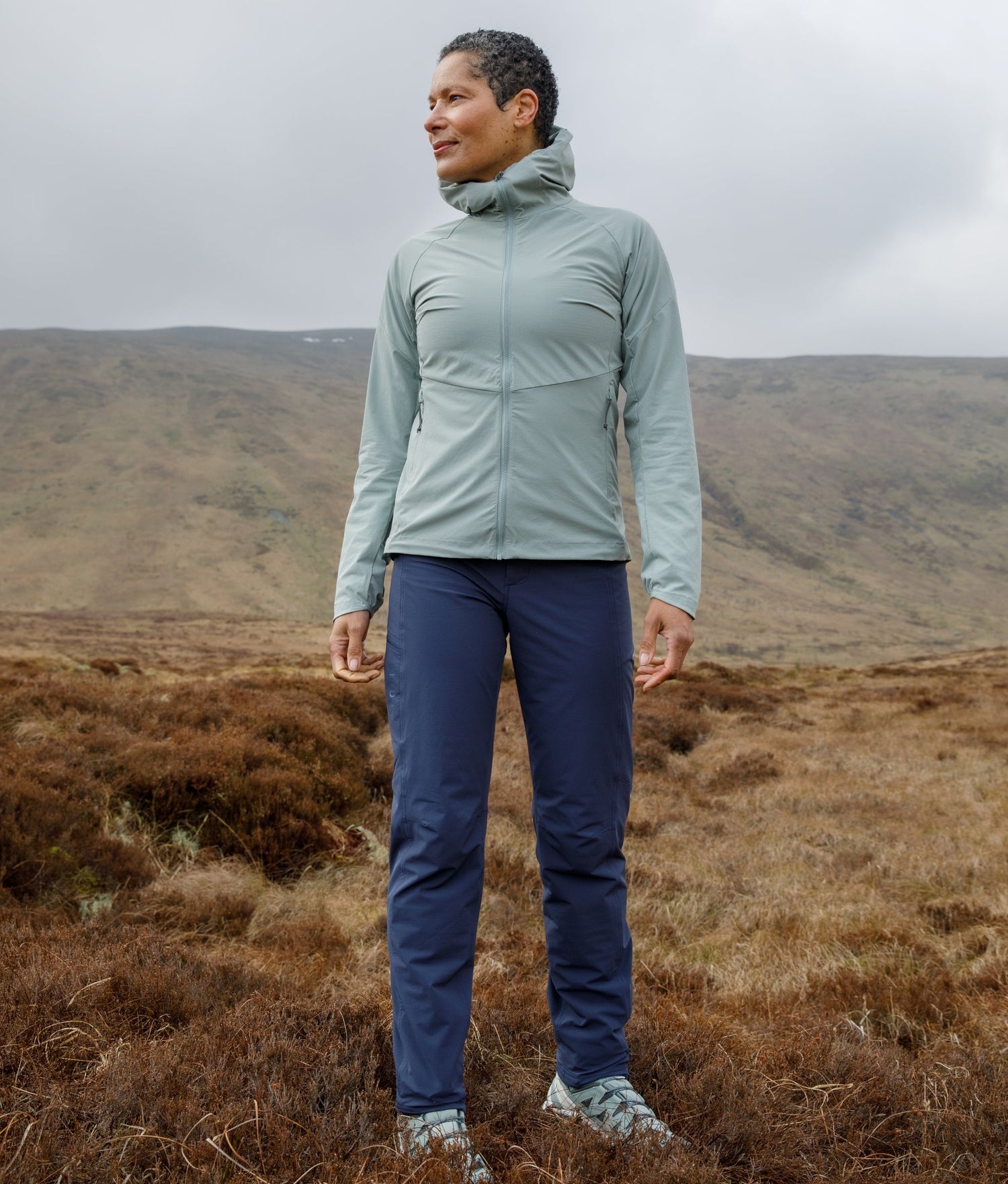 Person wearing a light green jacket and blue pants standing in a moorland landscape.