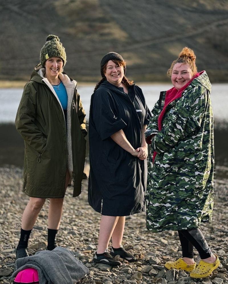 Three women standing by a body of water, wearing winter clothing.