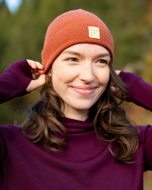 Person wearing a red beanie with a FINDRA logo, standing outdoors with trees in the background
