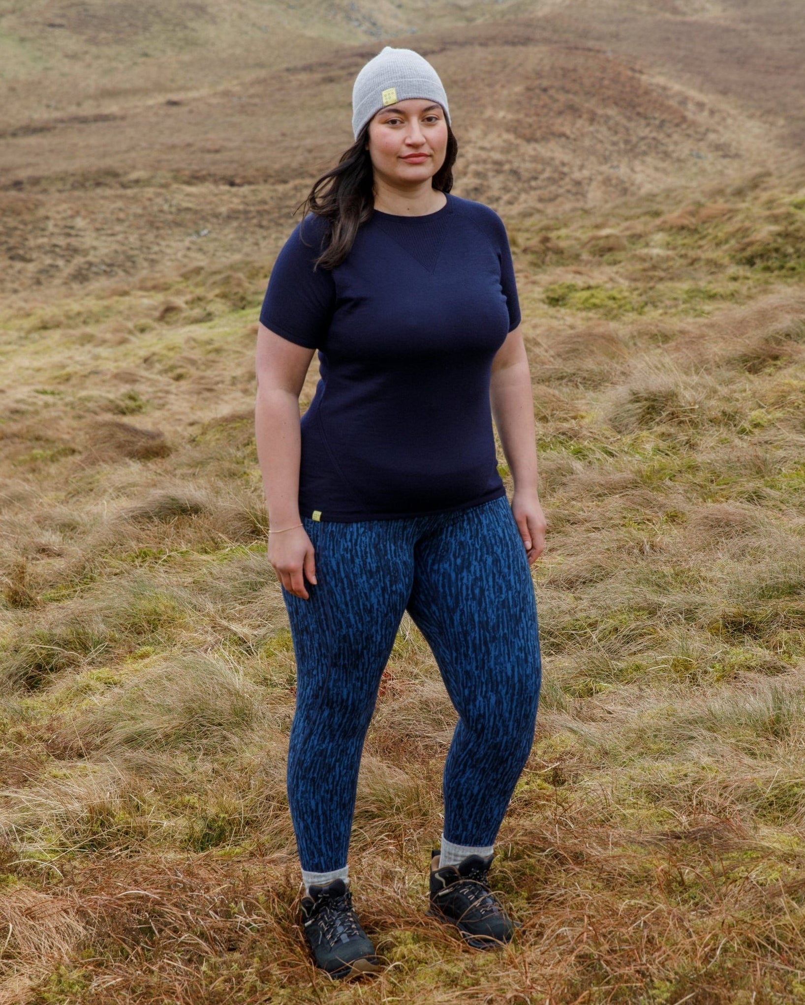Person wearing a navy t-shirt and blue patterned technical  leggings standing in a grassy field.