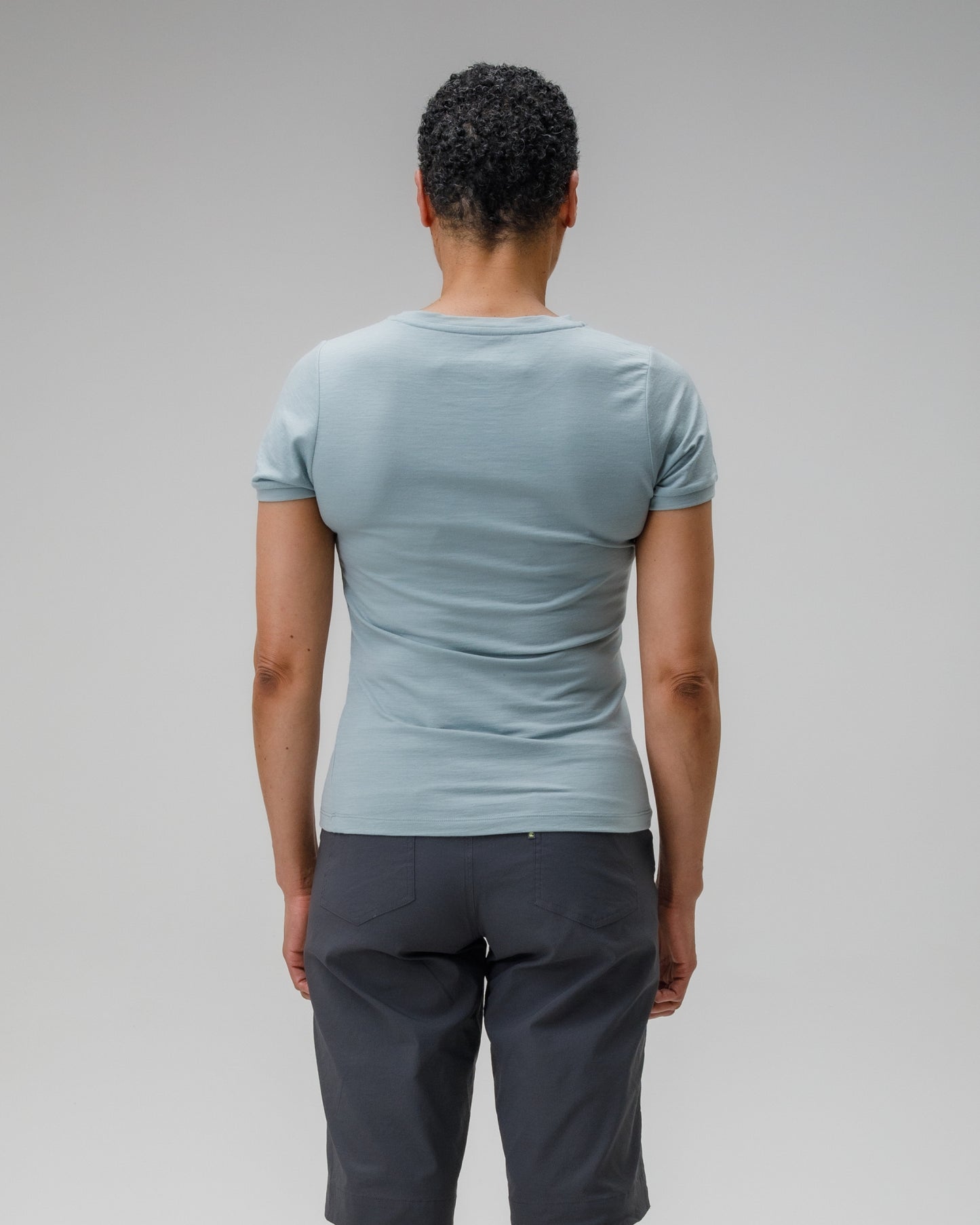 Person wearing a light blue t-shirt and dark gray pants on a plain background