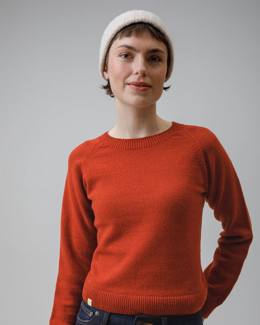 Person wearing an orange sweater and a white beanie against a plain background