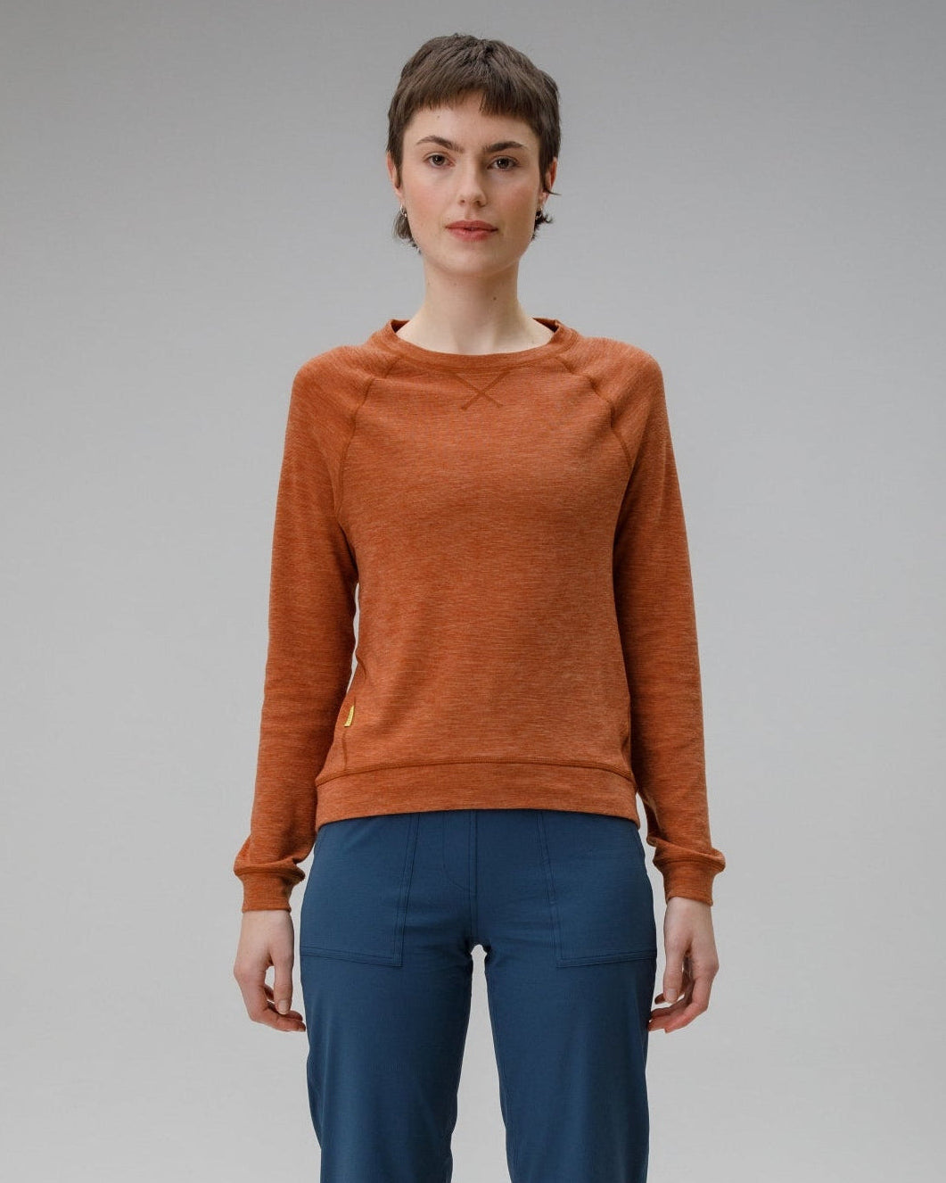 Person wearing a orange/brown sweater and blue pants on a grey background