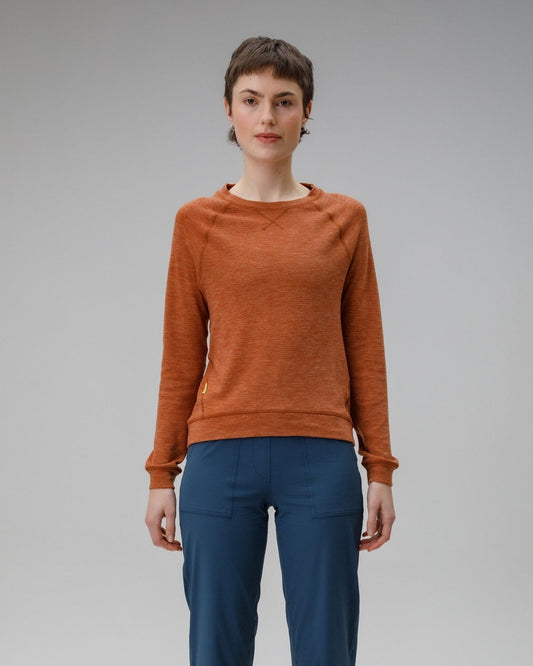 Person wearing a orange/brown sweater and blue pants on a grey background