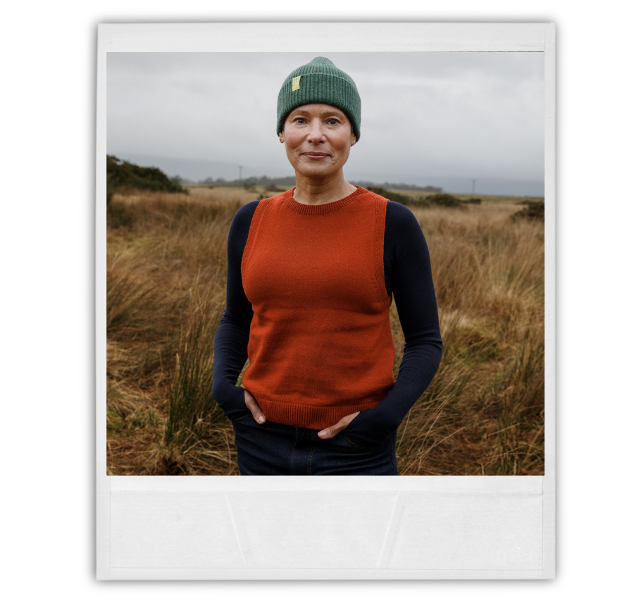 Person wearing a green beanie and orange sweater standing in a field